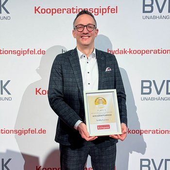 BVDAK Apothekenkooperation Preisverleihung Marc Hargarter hält eine Auszeichnung für kohlpharma vor einem Hintergrund mit BVDAK Apothekenkooperation