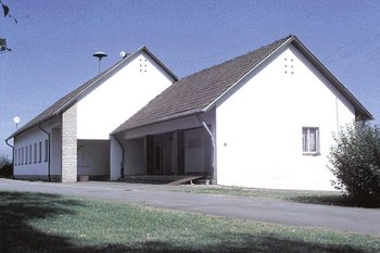 Kohlpharma Historie: Erster Firmensitz Erster Firmensitz von Kohlpharma in Zwergschule Borg mit weißen Wänden und braunem Dach unter blauem Himmel.