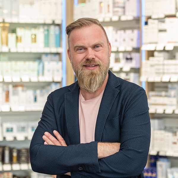 Apotheker Gutersohn im Gespräch Apotheker Gutersohn steht mit verschränkten Armen vor einem Regal voller Medikamente und lächelt freundlich in die Kamera.