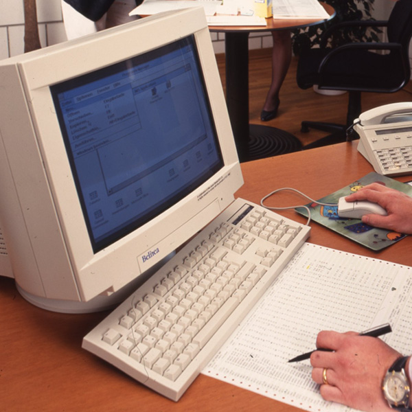 Computer Historie: Alte Technologie im Einsatz Computer Historie zeigt einen alten PC mit Tastatur und Maus auf einem Schreibtisch mit Dokumenten und einer Person.