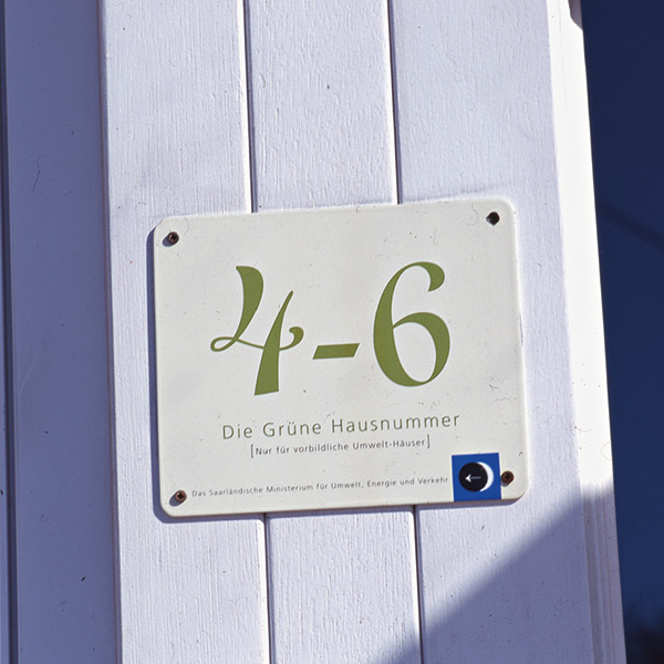 Gruene Hausnummer 4-6 Grüne Hausnummer 4-6 auf einem weißen Schild mit grünen Zahlen und Text auf einer Holzwand angebracht.