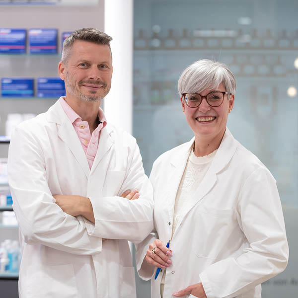 Zwei Apotheker im Labor Zwei Apotheker in weißen Kitteln stehen nebeneinander und lächeln in die Kamera.