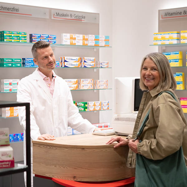 Apotheker und Patientin in der Apotheke Apotheker und Patientin stehen im Beratungsgespräch in der Apotheke ein Medikamentenregalen im Hintergrund.