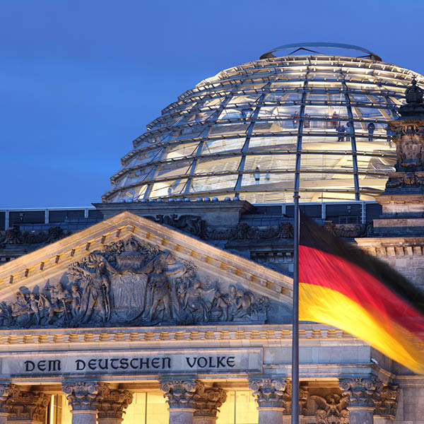 Die Reichstagskuppel bei Nacht mit deutscher Flagge und dem Inschrift Dem deutschen Volke am Eingang.